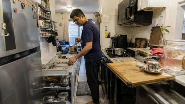 A cramped kitchen showing a pull-out storage organizer and wall storage system actively used during cooking